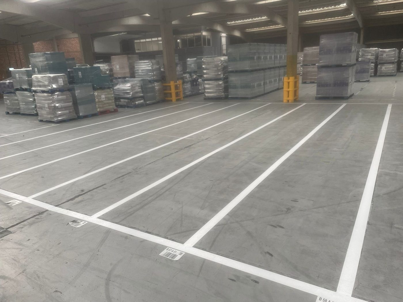 Same warehouse floor with crisp new white line markings defining aisles and bays