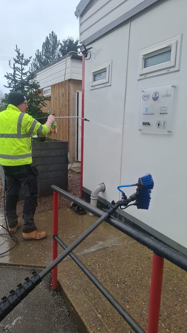 Eastrada team member in branded hi-vis pressure washing a building exterior using a water-fed pole system